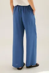 Pantalón de lino azul de corte recto y amplio, con cintura elastizada, cierre de cremallera y botón. Presenta detalles de pespunte blanco en los bordes de los bolsillos.