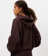 Hoodie de color marrón oscuro con diseño voluminoso tipo globo, capucha con cordón de ajuste, mangas largas abullonadas con pliegues y bolsillo canguro frontal.