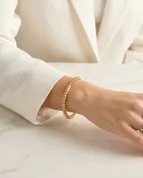 Pulsera esclava de acero con baño de oro, compuesta por pequeñas esferas texturizadas y un detalle central cilíndrico estriado.