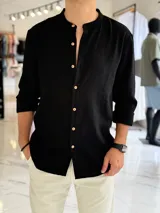 Camisa de lino color negro, con cuello mao y cierre frontal de botones en contraste. Presenta mangas largas con puños arremangados y diseño clásico.
