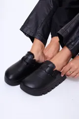 Sueco de cuero sintético negro con interior forrado en piel sintética. Presenta una tira ajustable con hebilla metálica en el empeine y una suela de plataforma dentada.