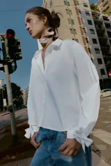 Camisa de cuello solapa y manga larga, con cierre frontal de botones y puños ajustables decorados con lazos del mismo tejido.