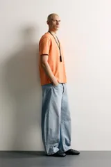 Jeans de denim de algodón color gris con efecto lavado, de corte relaxed barrel fit y tiro medio. Presenta diseño amplio con pinzas en las rodillas y costuras curvas, cierre frontal con botones y cinco bolsillos tradicionales.