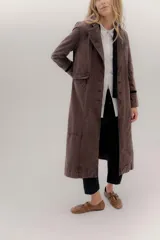 Tapado largo de jean azul oscuro, con cuello solapa y puños con detalle de cinta de terciopelo negro. Presenta costuras visibles que definen paneles y un logo bordado en la espalda.