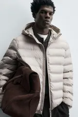 Campera puffer acolchada de corte regular fit en color negro, confeccionada en tejido técnico repelente al agua. Presenta cuello subido con capucha, cierre frontal de cremallera, mangas largas con puños elásticos y bolsillos laterales de vivo.