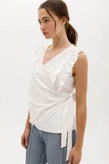 Musculosa cruzada de color beige, con escote en V y volados decorativos en los hombros y el frente.