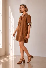 Vestido corto color marrón de lino, con cuello polo, cierre frontal parcial con botones y mangas tres cuartos con detalles de lazos en los puños y bolsillos laterales.