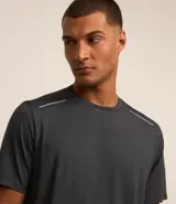 Remera deportiva masculina de manga corta con cuello redondo, confeccionada en tejido técnico con tecnología Dry para mayor transpirabilidad. Presenta detalles reflectantes en los hombros y un diseño liso en color verde melange.