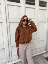 Campera de estilo bomber confeccionada en simil gamuza color marrón, con cuello camisero, cierre frontal oculto y puños elásticos.