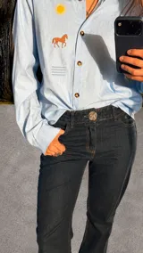 Pantalón vaquero de tiro bajo y corte recto en color bordó, con cierre frontal de botón metálico con diseño de caballito y bolsillos.