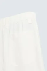 Pantalón de corte relajado confeccionado en tejido de cáñamo color blanco roto. Presenta cintura elástica con cordón interior ajustable, cierre frontal con botones, bolsillos laterales y un bolsillo trasero de plastrón.