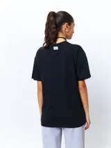 Remera negra de manga corta, corte oversize, con estampado frontal de una figura femenina de estilo asiático rodeada de flores blancas y verdes.
