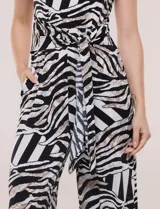 Enterito cropped con caída fluida, escote redondo, mangas cortas y pantalón ancho tipo wide leg. Presenta un lazo frontal para anudar en la cintura, bolsillos laterales y cierre posterior invisible. Cuenta con estampado animal print tipo cebra.