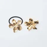 Set de accesorios para el pelo compuesto por una colita elástica negra con aplique de flor dorada texturizada y un clip tipo cocodrilo con aplique de flor dorada lisa.