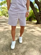Conjunto deportivo compuesto por una remera de manga corta y un short lila con cordón de ajuste blanco.