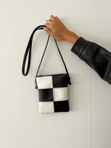 Monedero pequeño con correa larga, con diseño de tablero de ajedrez en blanco y negro.