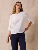 Blusa de gasa con estampado geométrico en tonos negro, gris y celeste. Tiene cuello redondo y mangas 3/4 amplias con abertura y botón.