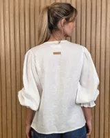 Camisa color beige de lino con mangas abullonadas tres cuartos y cierre frontal mediante múltiples lazos para atar.